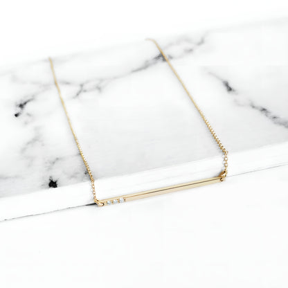 yellow gold thin bar necklace set with three tiny white diamonds