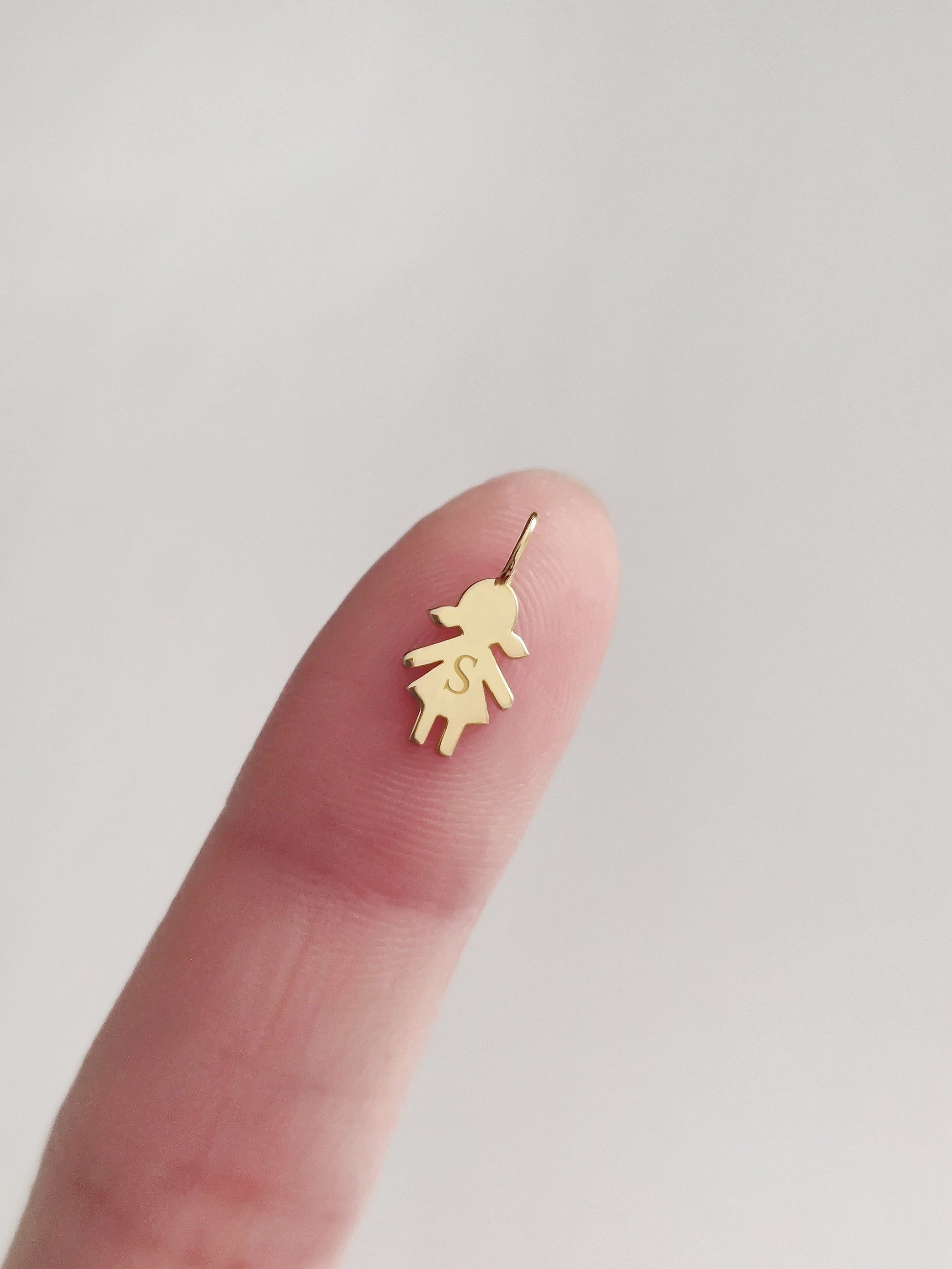 close up of a fingertip holding a tiny gold girl outline charm engraved with an initial for size reference